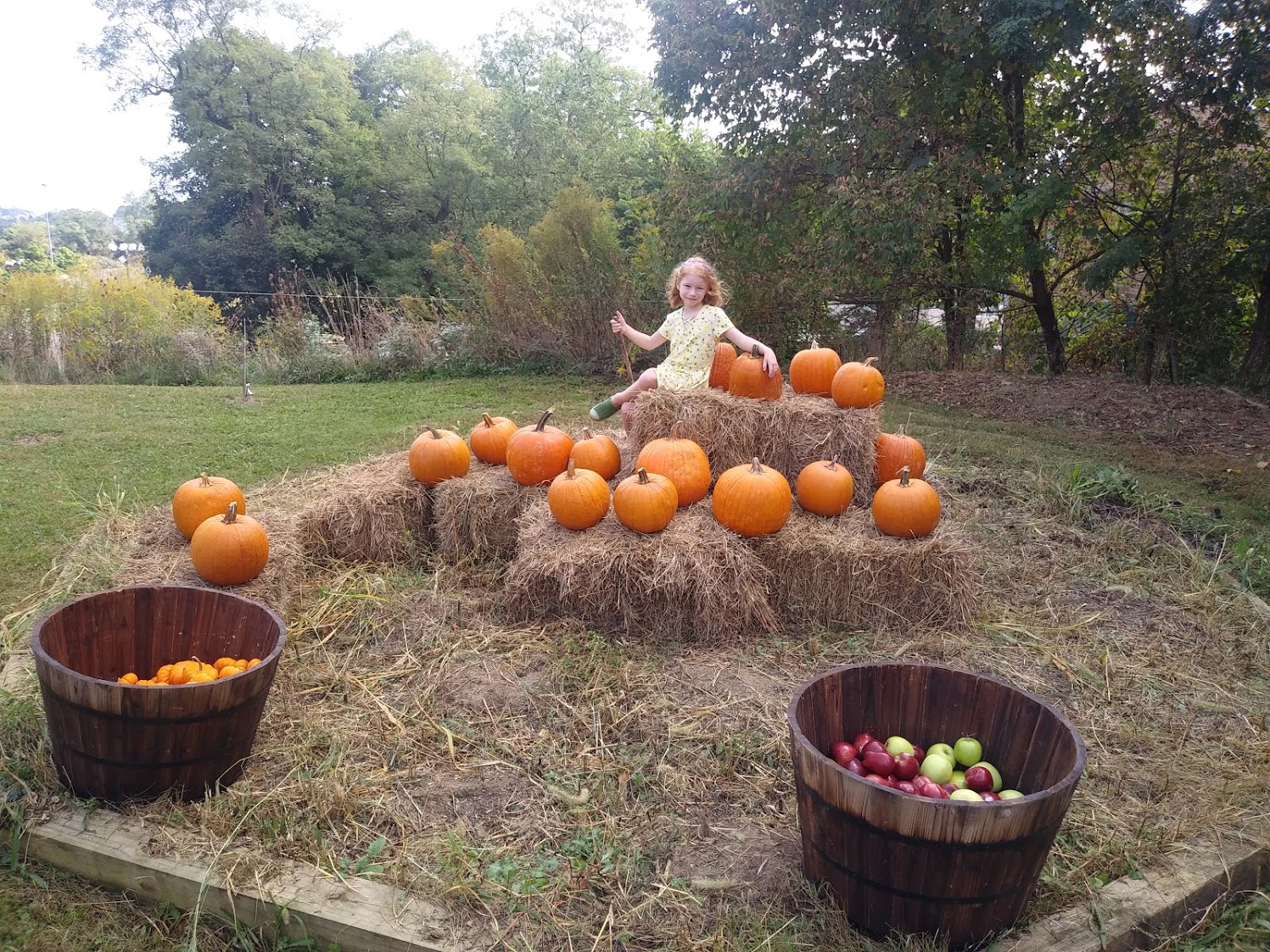 A girl sitting on hay bales with pumpkins.